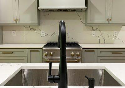 View from kitchen island past sink and looking onto tan cabinetry and gas range with hood fan.