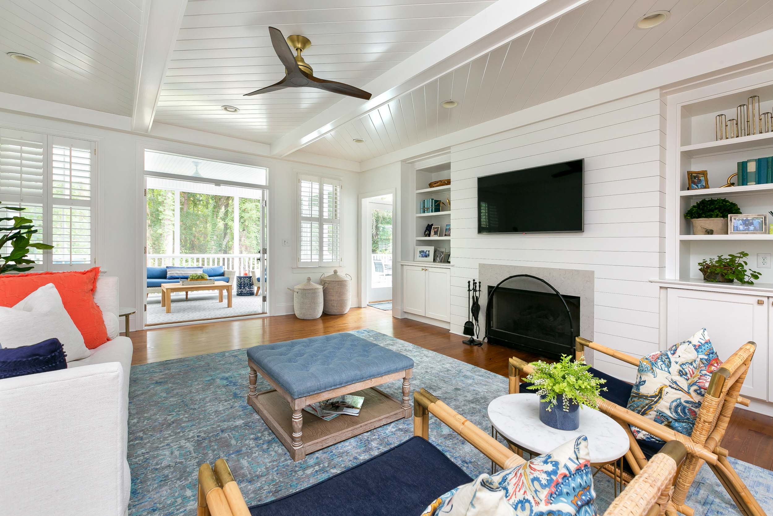 Open floor plan view of living room looking out to screened porch, ornate cieling, ship lap accent wall and fireplace.