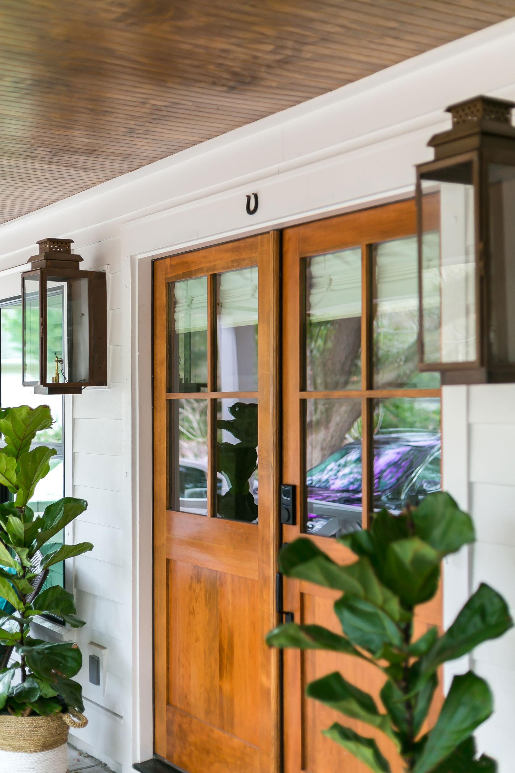 Warm wood front doors with large windows, oil burning lantern style sconces and dark stained beadboard ceiling.