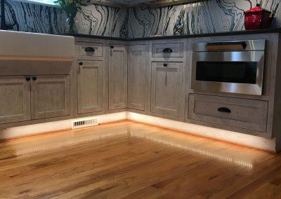 Zebra marbled tile backsplash in a kitchen with under-cabinet lighting at the base and large farmhouse sink, inlaid convection oven built into the custom cabinetry.