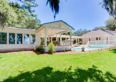 Pool house and decks wrapping around pool patio view from edge of yard under spanish moss dripped oaks.