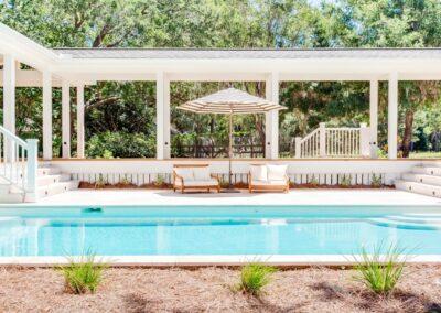 Pool deck with two love seats, landscaping and beautiful aqua blue pool in foreground.