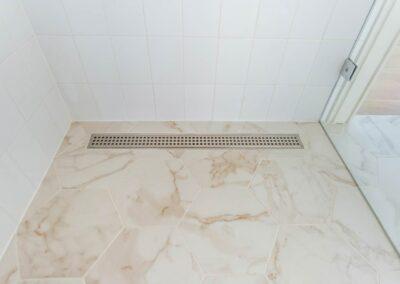 Hexagon marbled tile in shower with a long thin shower drain and subway tile walls with glass door.