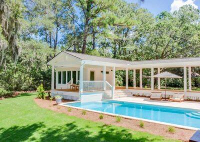 Cabana and pool deck with landscaping and tree line behind.