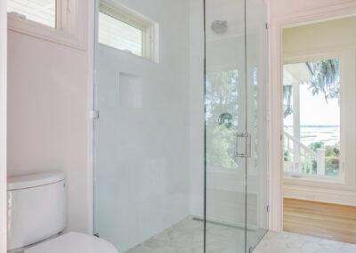 Glass surrounded stall shower with marsh view out bathroom door.