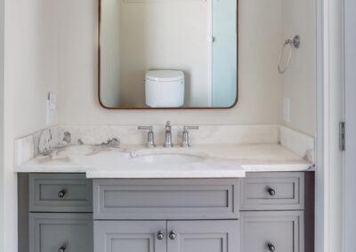 Gray and white vanity cabinet and mounted mirror with sconces.