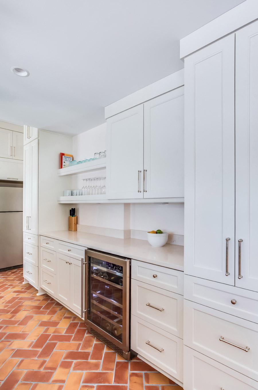 Custom kitchen cabinetry with wine fridge, stainless appliances, open shelving and brick floor.