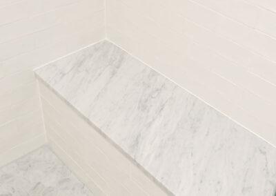 Custom tiled stall shower with hexagonal tile floor, single marble slab bench and subway tile walls.