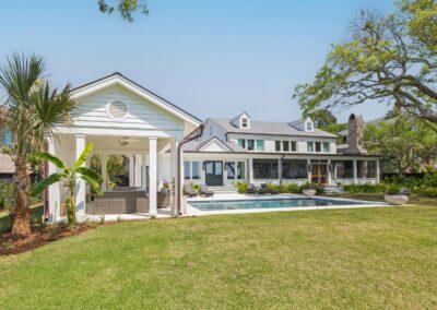 Rear view of home with cabana, pool deck and screened porch on subtropical grounds with oak tree, palmetto and other tropical plants.