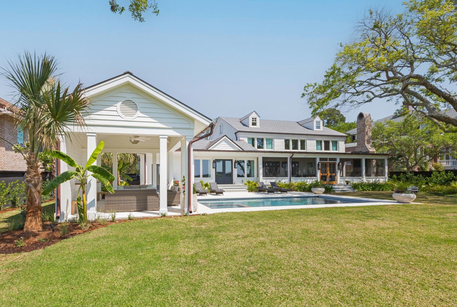 Rear view of home with cabana, pool deck and screened porch on subtropical grounds with oak tree, palmetto and other tropical plants.