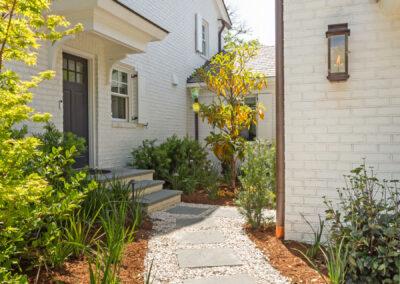 Pavers and pea gravel leading to side door on custom white brick home.