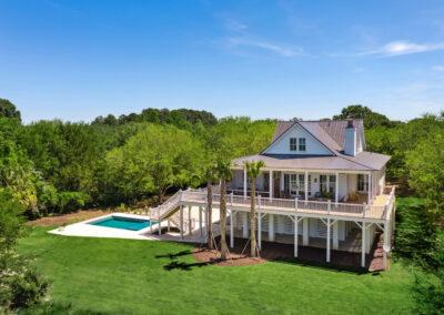 Aerial view of custom home with multiple roof pitches, near wrap around decks and pool with deck surrounded by green trees