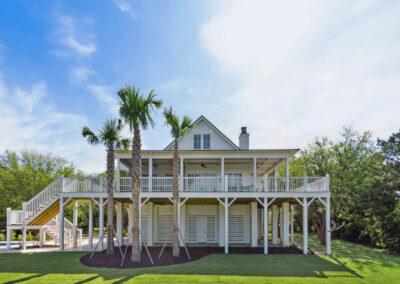 Back view of house, elevated with enclosed ground level, large back deck and three palmetto trees newly planted.