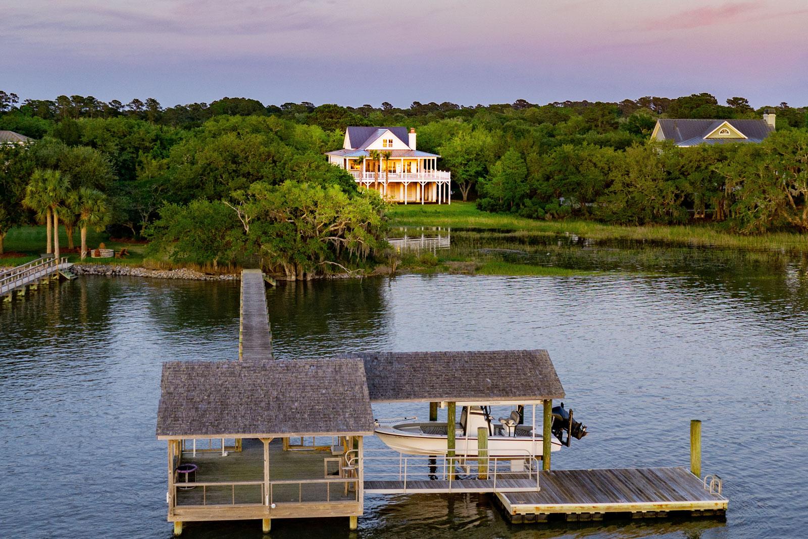 Beautiful dock with covered seating, floating dock and covered boat lift leading back to property with custom home in distance.