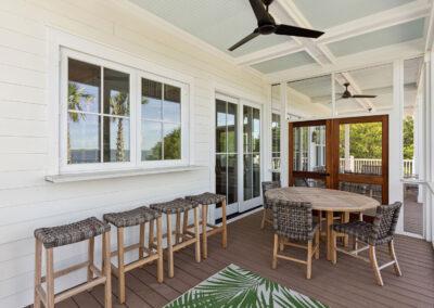 Custom built back porch with kitchen window bar and stools, sliding door to inside, table and chairs and double screen doors leading to covered porch beyond.