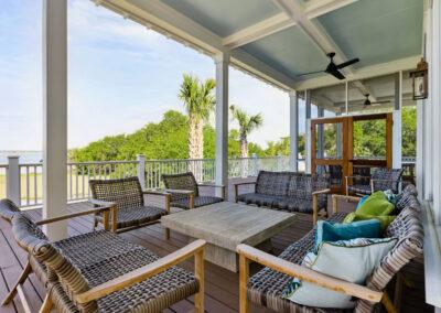 Scenic view from covered, open-air back porch of custom built home overlooking river and march with seating for 8 around natural wood coffee table.