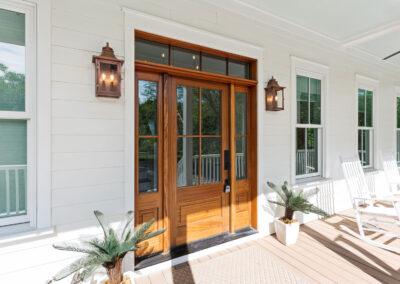 Close up of front door on white sided home, beautiful lanterns and white rocking chairs soaking up the late day sunlight.