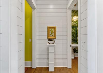 Hallway view with ship lap walls looking into two rooms, one on either side with contrasting lime green paint and jungle foliage wallpaper in powder room.