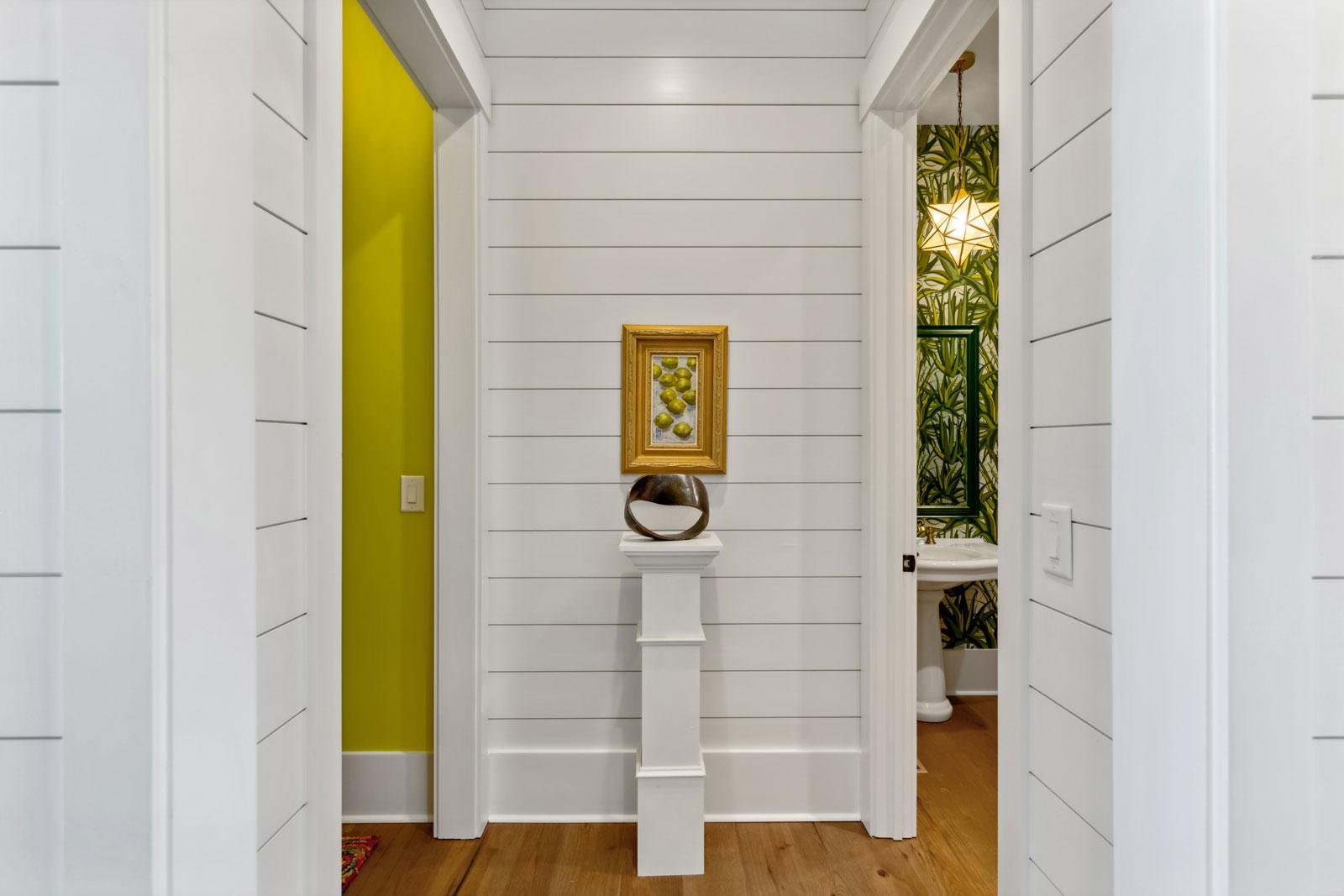 Hallway view with ship lap walls looking into two rooms, one on either side with contrasting lime green paint and jungle foliage wallpaper in powder room.