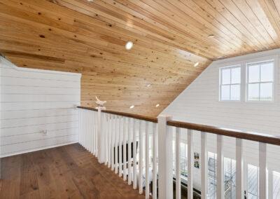 Upstairs loft looking out, windows adjacent and great room below - natural wood paneled ceiling and ship lap walls.