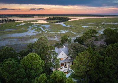 Aerial view of beautiful Kiawah Island custom home and the marsh out behind it around sunset with light fading in the background.