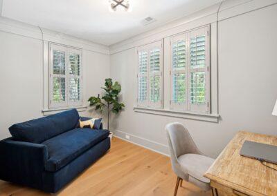 Small room home office with beautifully ornate moulding around ceiling and windows. Plantation shutters on the inside. Warm light colored hard wood floors.
