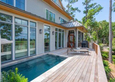 View of pool deck looking back toward the house with large floor to ceiling windows and screened in porch in the background.