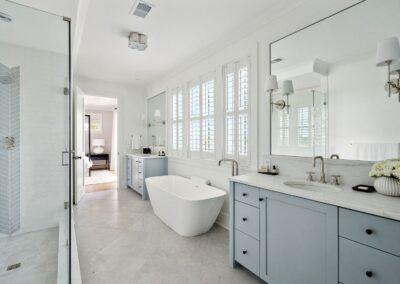 beautiful and large master bathroom with dual vanities separated by a free standing deep soaking tub and three panel windows. custom stall shower on opposite side and a view into the bedroom in the background.