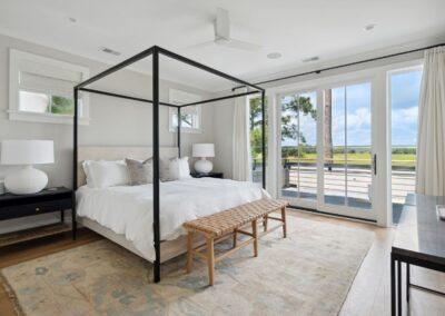 Beautiful and bright bedroom with sliding glass door to open air deck overlooking the marsh. Four-poster bed with neutral decor and warm hard wood floors.