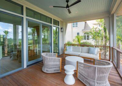 Covered porch with large sliding glass door leading inside. Comfortable, modern and coastal styled furnishings on a warm wooden stained deck.