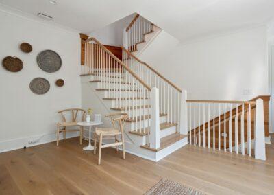 Second floor of custom home. Landing with table and a chairs and light wood and painted white stair leading up and down.