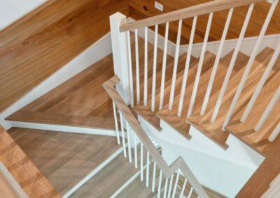 Shot from above of light wood and painted white stair spiraling down to next level of custom home.