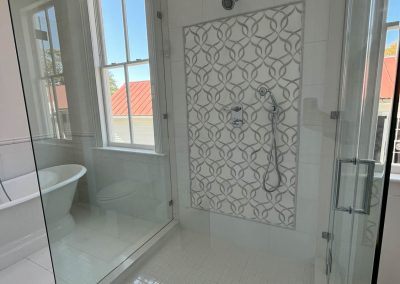 A remodeled bathroom in a historic Charleston home with a glass-enclosed stall shower and a soaking tub that can be seen in the background.